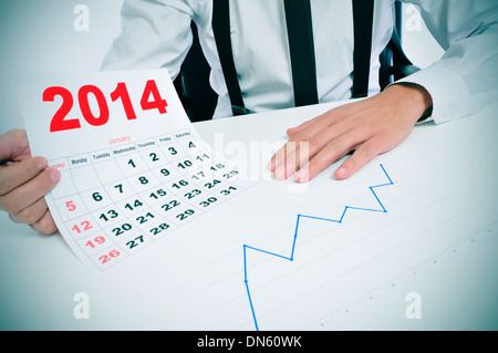 Imprenditore seduto su una scrivania con un grafico e che mostra un calendario 2014 Foto Stock