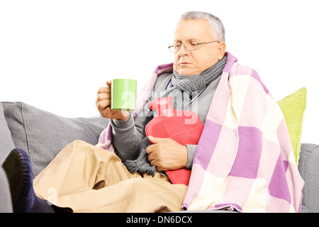 Ill uomo di mezza età su un divano coperto con una coperta di bere il tè caldo Foto Stock