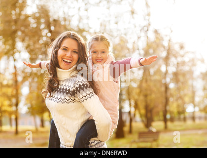 Madre dando figlia piggyback ride nel bosco in autunno Foto Stock