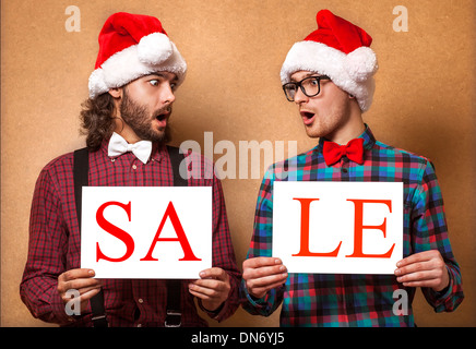 Natale, X-mas, persone, pubblicità, vendita concetto - happy due uomo in santa helper hat con vuoto scheda bianca. Hipster stile. Foto Stock