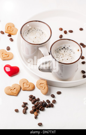 Traino di tazza di cappuccino servito con spezie e cookie come cuori e un cuore rosso su bianco tessile. Vedere serie Foto Stock