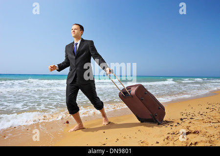 Giovane imprenditore nel soddisfare a camminare su una spiaggia di sabbia con i suoi bagagli Foto Stock