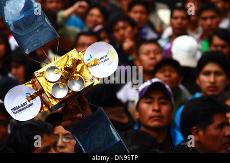 LA PAZ, Bolivia, il 20 dicembre 2013. Una mano trattiene aloft un modello di Tupac Katari (Bolivia il primo satellite per comunicazioni) a un evento a celebrare il suo lancio dal XiChang stazione spaziale in Cina in Plaza Murillo. Il Tupac Katari satellite (chiamato dopo un eroe indigeno che ha condotto una sollevazione contro gli spagnoli) è stato costruito per un costo di circa $300 milioni. Credito: James Brunker / Alamy Live News Foto Stock