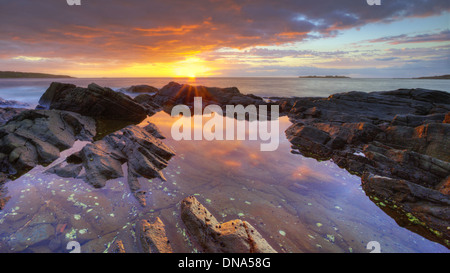 Alba sulle rocce con acqua che riflette il cielo illuminato Foto Stock