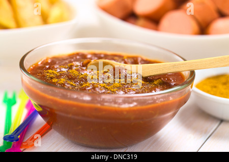 Curry ketchup salsa fatta immergere le salsicce fritte e patatine fritte servite in recipiente di vetro con il cucchiaio di legno Foto Stock