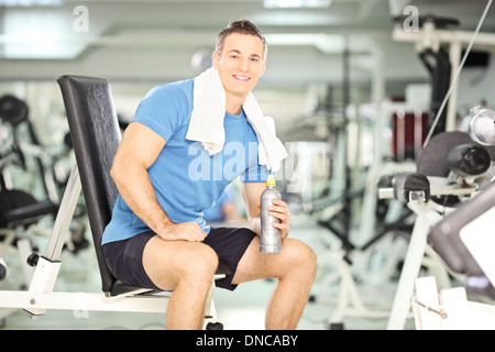 Uomo sorridente seduto su una panchina acqua potabile dopo esercizio in palestra per il fitness Foto Stock