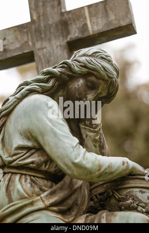 Vecchia lastra tombale statua del triste pensare la donna accanto a una croce Foto Stock