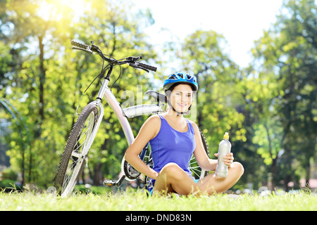 Femmina giovane biker seduto su un prato accanto alla sua bici in un parco Foto Stock