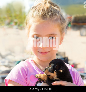 Blonde kid ragazza che gioca con il cucciolo di cane sorridente con gli occhi blu Foto Stock