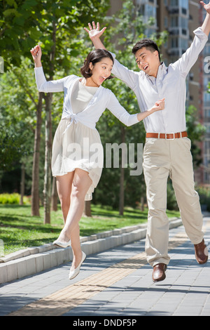 Emozionato coppia giovane jumping in metà di aria esterna Foto Stock