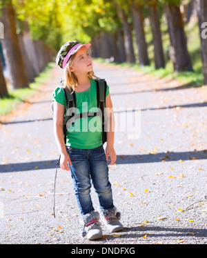 Blonde explorer kid ragazza camminare con zaino in autunno alberi via Foto Stock