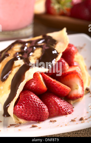 Crêpe riempito con fragole fresche e salsa al cioccolato sulla sommità guarnita con scaglie di cioccolato sulla piastra Foto Stock