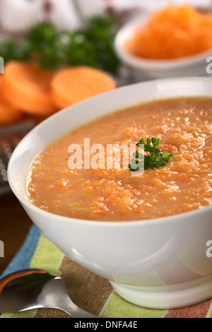 La carota crema zuppa di carote grattugiate e guarnito con una foglia di prezzemolo (messa a fuoco selettiva, concentrarsi sulle foglie di prezzemolo) Foto Stock