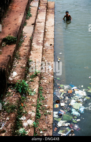 Giovane uomo locale di balneazione in cucciolata inquinato fiume disseminato in India Foto Stock