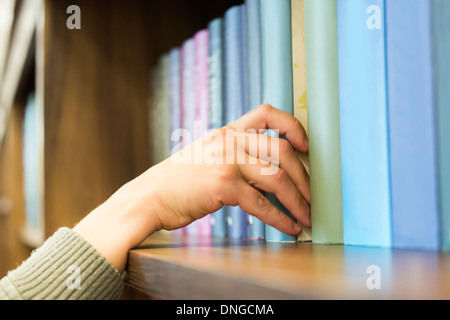 La mano tirando un libro dallo scaffale. Colori blu libri Foto Stock