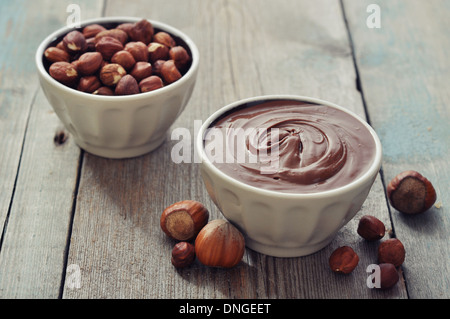 Crema nocciola nella ciotola in ceramica con nocciole su sfondo di legno Foto Stock