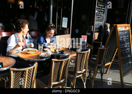 Persone di mangiare al cafè sul marciapiede con circolare tradizionale i tavoli e le sedie di vimini e menu esposti sulla lavagna Foto Stock