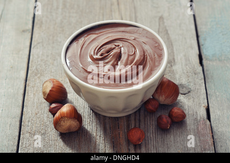 Crema nocciola nella ciotola in ceramica con nocciole su sfondo di legno Foto Stock