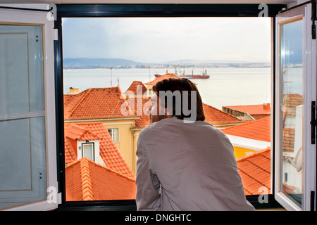 Giovane uomo che guarda alla splendida vista di Lisbona dalla finestra aperta - Vista posteriore. Foto Stock