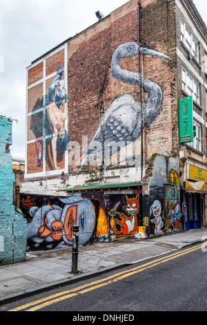 Arte di strada. Uomo che fa con una mano sola handstand da Martin Ron, Heron da ROA e pelliccia tre-eyed neonati da Alex faccia in Hanbury Str Foto Stock