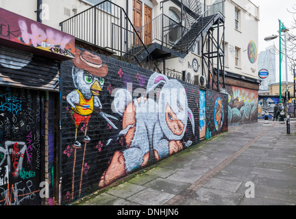 Arte di strada da Alex faccia. Un uccello nel cappello e maglietta gialla taglia le pellicce di tre eyed baby in bunny suit con cesoia, Pedley Str., Londra Foto Stock