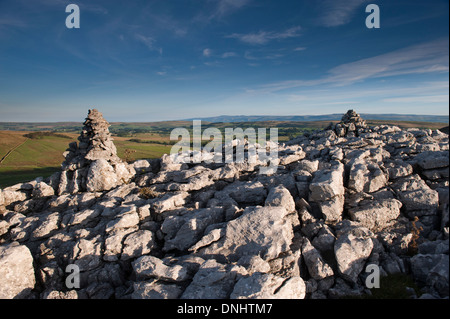 Calcare Cairn cattura primi raggi di sole sulla estremità cadde nuvole, una zona di pavimentazione di pietra calcarea vicino Ravenstonedale, Cumbria. Foto Stock