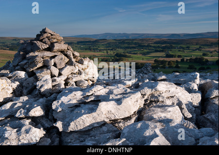 Calcare Cairn cattura primi raggi di sole sulla estremità cadde nuvole, una zona di pavimentazione di pietra calcarea vicino Ravenstonedale, Cumbria. Foto Stock