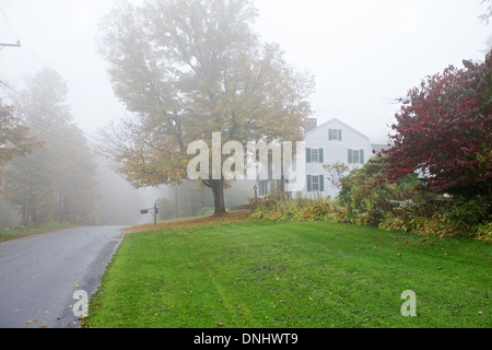 Foschia mattutina, Autunno / caduta delle foglie. Paese vista laterale con la casa di legno con un auto sulla strada Foto Stock