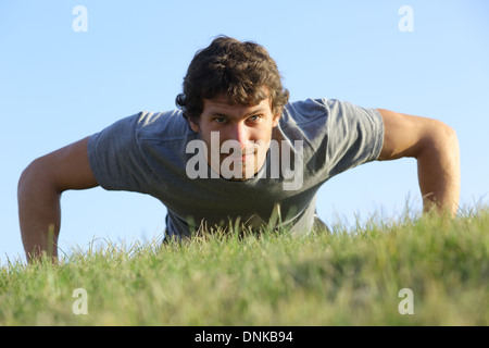 Close up di un uomo che fa pushups sull'erba con l'orizzonte in background Foto Stock