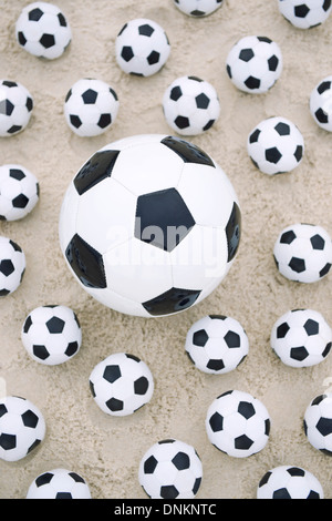 Molti piccoli palloni da calcio circondano grande pallone da calcio brasiliano sulla spiaggia di sabbia Foto Stock