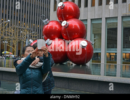 Un asiatico madre e figlio in Midtown Manhattan in posa per un telefono cellulare fotografia di fronte ad un edificio di decorazioni di Natale Foto Stock