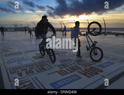 Ragazzi adolescenti di eseguire trucchi di bicicletta sulla commedia di Blackpool moquette o pavimentazione al tramonto, dopo la scuola. Lancashire, Regno Unito Foto Stock