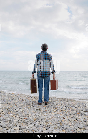 Retro dell'uomo con le valigie sulla spiaggia rocciosa, Frontignan, Francia Foto Stock