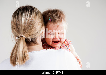 Oltre la spalla di Madre tenendo il pianto Baby girl, Studio Shot Foto Stock