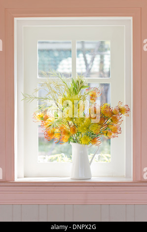 Fiori artificiali in vaso bianco accanto alla finestra bianca. Foto Stock