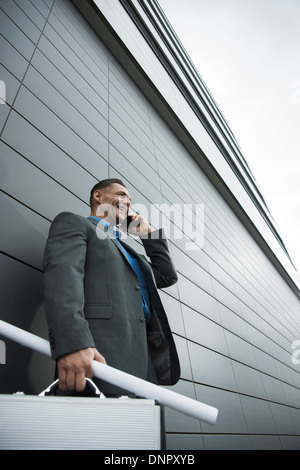 Imprenditore in piedi nella parte anteriore della parete di edificio tramite telefono cellulare, Mannheim, Germania Foto Stock