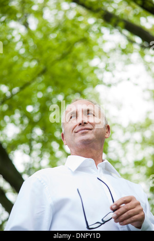 Close-up ritratto di uomo maturo azienda corno-occhiali bordati nel parco, Mannheim, Germania Foto Stock