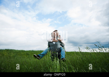 Coppia matura nel campo di erba, uomo dando piggyback ride per donna, Germania Foto Stock