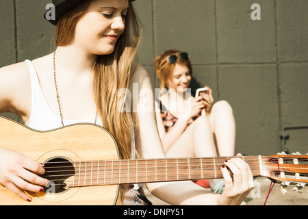 Giovani donne seduti all'aperto, appendere fuori e suonare la chitarra, Mannheim, Germania Foto Stock