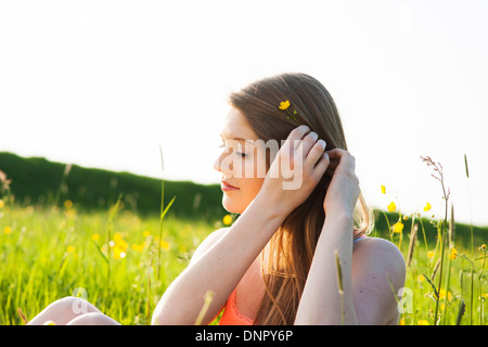 Giovane donna seduta nel campo immissione fiore nei capelli, Germania Foto Stock