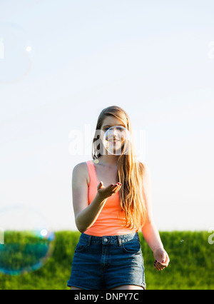 Giovane donna camminare in campo giocando con bolle, Germania Foto Stock