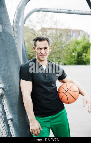 Ritratto di uomo maturo permanente sulla outdoor pallacanestro, Germania Foto Stock