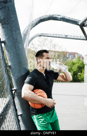 Uomo maturo permanente all'aperto sul campo di pallacanestro di bere una bottiglia di acqua minerale, Germania Foto Stock