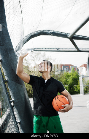 Uomo maturo permanente sulla outdoor pallacanestro versando una bottiglia di acqua sul viso, Germania Foto Stock