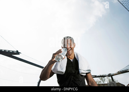 Uomo maturo con asciugamano attorno al collo, bere una bottiglia di acqua minerale e guardando la telecamera, Germania Foto Stock