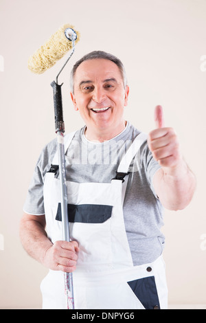 Ritratto del pittore dando pollice in alto e di contenimento del rullo di vernice, Studio Shot Foto Stock