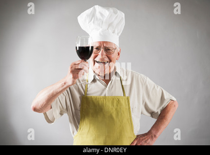 Senior Uomo con vino rosso che indossa il grembiule e dallo Chef Hat, Studio Shot Foto Stock