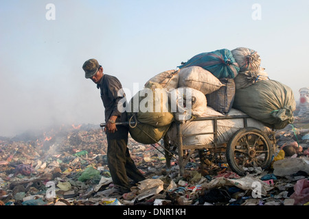 Un lavoratore di sesso maschile cale di materiale riciclabile con un carrello di acciaio presso il pungo Meanchey discarica in Phnom Penh Cambogia. Foto Stock
