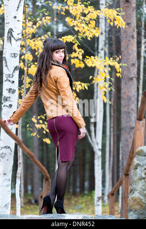 Affascinante ragazza nel bosco in autunno si trasforma in piedi sui gradini. Foto Stock