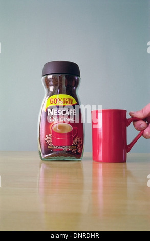 Vasetto di Nescafe originale di caffè istantaneo e uomo caucasico la mano di prelevare un boccale rosso modello rilasciato Foto Stock
